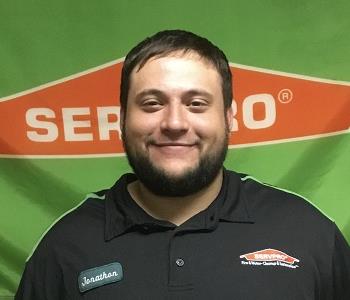bearded male employee without glasses standing in front of a SERVPRO logo'd banner