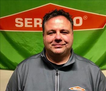male employee in front of SERVPRO logo banner smiling