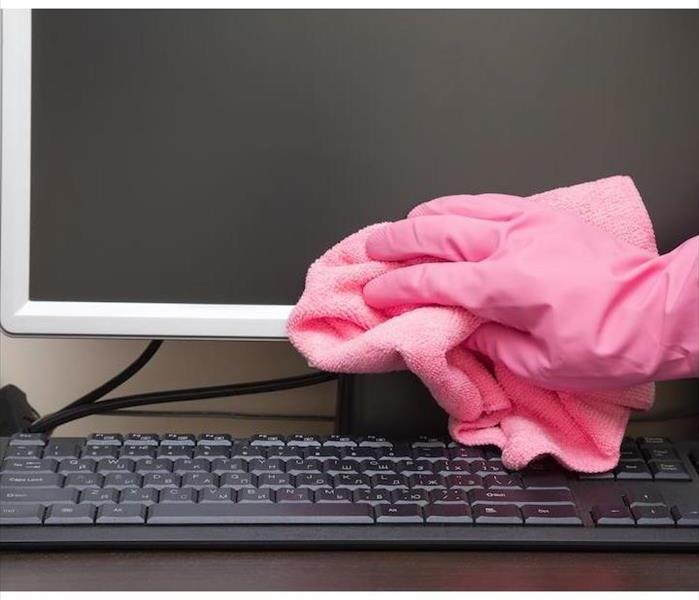 hand with a pink glove wiping a computer monitor with a pink rag